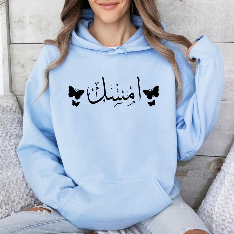 Personalised Arabic Name Butterfly Hoodie featuring elegant Arabic typography designed to transform your chosen name into a meaningful and stylish piece of wearable art. The combination of flowing Arabic calligraphy and delicate butterfly details creates a premium personalised garment that celebrates culture, identity, beauty, and individuality. Perfect for customers searching Arabic typography hoodies, personalised Arabic clothing, custom Arabic name apparel, Islamic fashion, Muslim women clothing, and uni