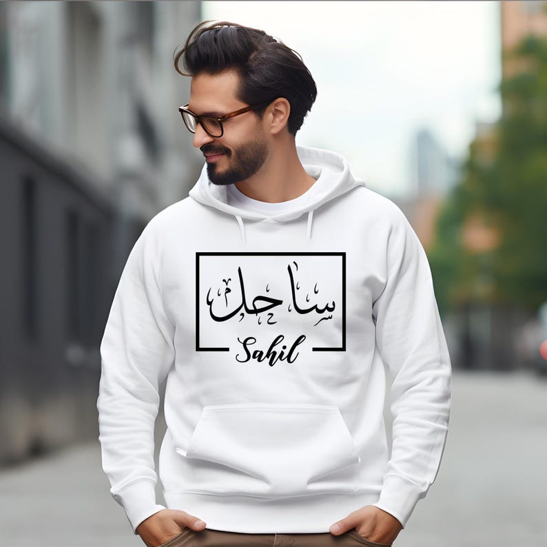 Elegant personalised Arabic name hoodie showcasing a premium gold Arabic calligraphy design positioned within a clean geometric frame. The minimalist layout combines traditional Arabic script with modern typography to create a sophisticated and eye-catching appearance. Printed on a black hoodie for maximum contrast and visual impact, the design offers a luxurious aesthetic while maintaining simplicity, making it ideal for lovers of personalised Arabic artwork.