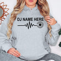 Designed for DJs, remix artists, vinyl collectors and music enthusiasts, this personalised DJ Name Heartbeat Hoodie celebrates music culture with a custom name, heartbeat waveform and vinyl record design. Professionally printed in the UK by TeezoraPrints.