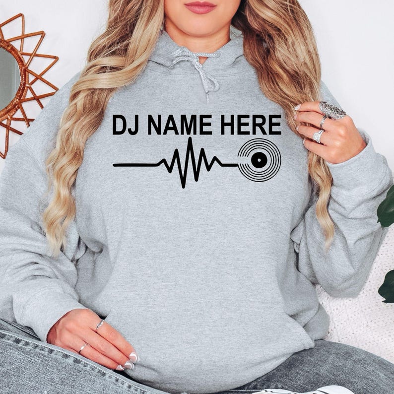 Designed for DJs, remix artists, vinyl collectors and music enthusiasts, this personalised DJ Name Heartbeat Hoodie celebrates music culture with a custom name, heartbeat waveform and vinyl record design. Professionally printed in the UK by TeezoraPrints.