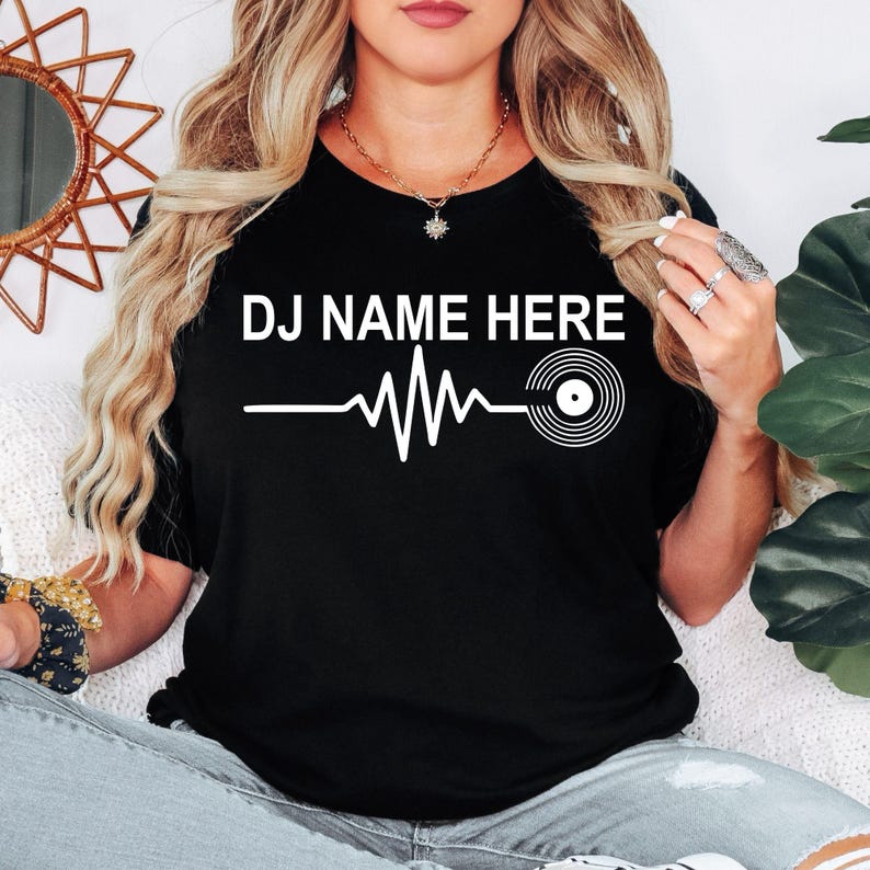 Personalised DJ Name Heartbeat T-Shirt featuring a custom DJ name, heartbeat waveform and vinyl record graphic. Designed for DJs, music producers, club performers and electronic music lovers who want a stylish personalised tee. Professionally printed in the UK by TeezoraPrints using premium-quality fabric for exceptional comfort, durability and everyday wear.