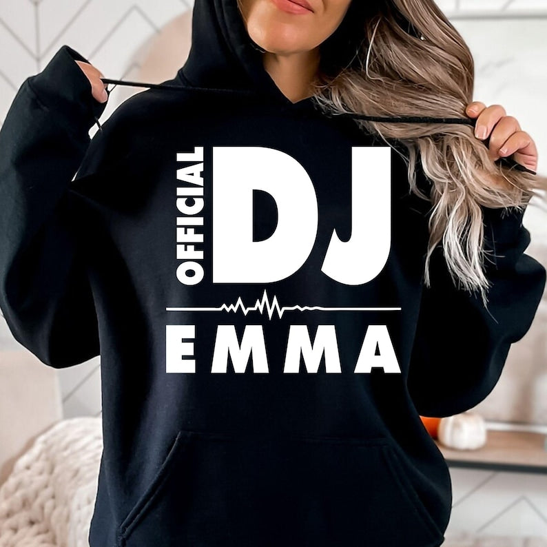 Personalised Official DJ Heartbeat Hoodie featuring a custom name, bold Official DJ typography and a heartbeat waveform graphic. Designed for professional DJs, music producers, club performers and electronic music lovers who want to represent their passion with a premium personalised hoodie. Professionally printed in the UK by TeezoraPrints using high-quality materials for warmth, comfort and long-lasting durability.
