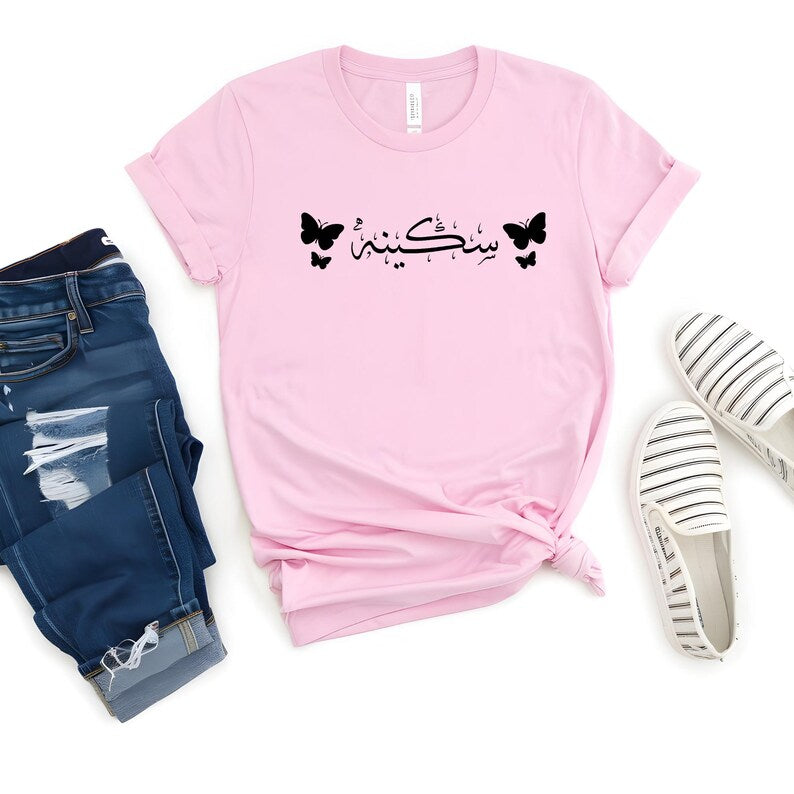 Personalised Arabic Name Butterfly T Shirt designed for Muslim women who appreciate modest fashion, personalised clothing, and elegant Arabic typography. Featuring custom Arabic calligraphy and beautiful butterfly artwork, this premium t shirt offers a stylish combination of comfort, identity, culture, and contemporary fashion. Perfect for everyday wear, family gatherings, Eid celebrations, Ramadan events, university life, travel, casual outings, and meaningful personalised gifting occasions throughout the 