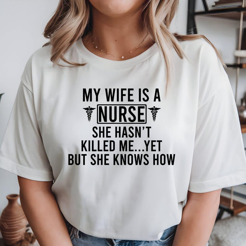 My Wife Is A Nurse She Hasn't Killed Me Yet But She Knows How T Shirt created for nurses, registered nurses, healthcare professionals, hospital staff, medical workers, supportive husbands, nursing families, and anyone who enjoys medical humour. Featuring bold nursing typography with medical symbols, this premium nurse-themed graphic tee from Teezora Prints delivers exceptional comfort, premium print quality, and stylish everyday fashion for proud nursing families.
