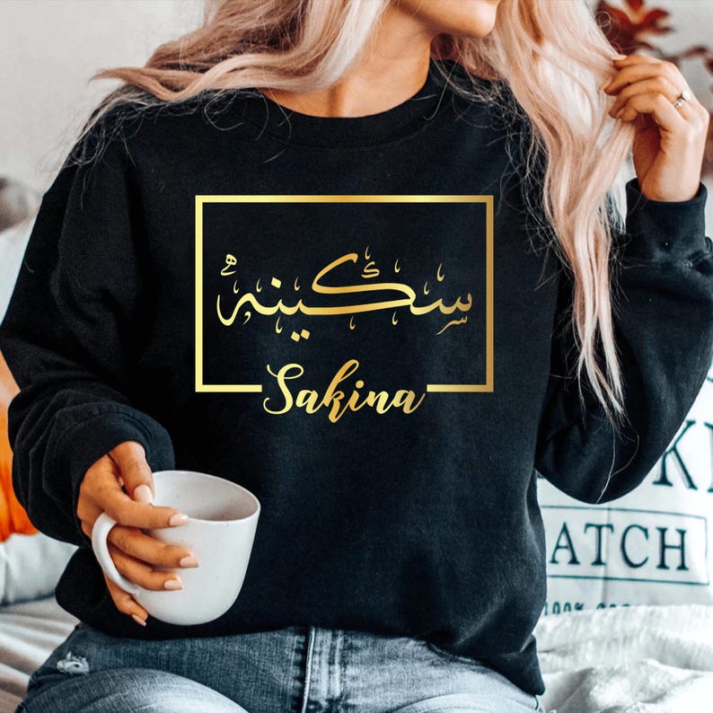 Personalised Arabic Calligraphy Name Sweatshirt featuring elegant Arabic script and custom name personalisation. Premium unisex sweatshirt designed with beautiful Arabic typography and minimalist styling, creating a meaningful personalised clothing piece. Perfect for Muslim women seeking stylish Islamic fashion, personalised apparel, and elegant Arabic-inspired clothing suitable for everyday wear and special occasions.