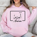 Elegant personalised Arabic name hoodie showcasing a premium gold Arabic calligraphy design displayed within a modern geometric frame. The minimalist composition blends traditional Arabic script with contemporary typography to create a sophisticated and eye-catching appearance. Printed on a black hoodie for maximum visual contrast, the luxurious gold lettering enhances the overall design while maintaining a clean and timeless aesthetic suitable for all ages.