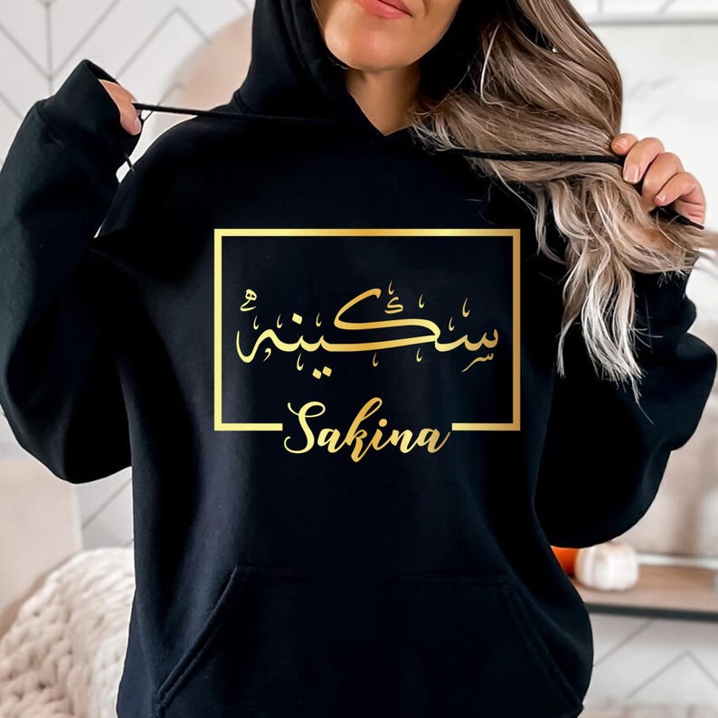1. Audience-Focused ALT
Personalised Arabic Name Hoodie designed for Muslim women, Arabic culture enthusiasts, and anyone seeking meaningful personalised clothing. This elegant black hoodie features a custom Arabic calligraphy name design printed in luxurious gold within a minimalist frame. Perfect for daughters, sisters, wives, mothers, friends, and loved ones who appreciate personalised apparel that combines identity, culture, comfort, and timeless style while expressing individuality through elegant Arab