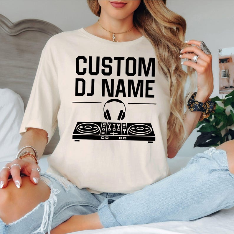 Express your passion for music with this personalised Custom DJ Name shirt featuring a professional DJ controller and headphones graphic. Whether mixing tracks, performing live, producing music or attending festivals, this premium t-shirt delivers all-day comfort and standout style. Every shirt is proudly printed in the UK by TeezoraPrints using premium materials.