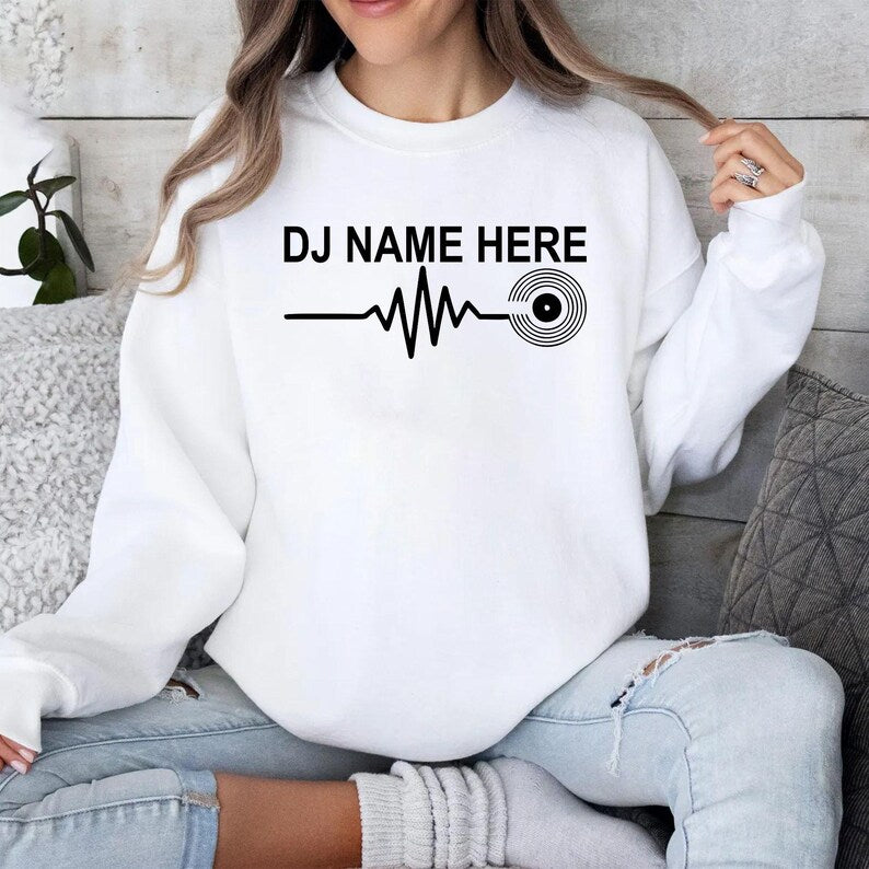 Personalised DJ Name Heartbeat Sweatshirt featuring a custom DJ name, heartbeat waveform and vinyl record graphic. Designed for DJs, music producers, club performers and electronic music lovers, this premium unisex crewneck is professionally printed in the UK by TeezoraPrints for exceptional comfort, warmth and everyday style.