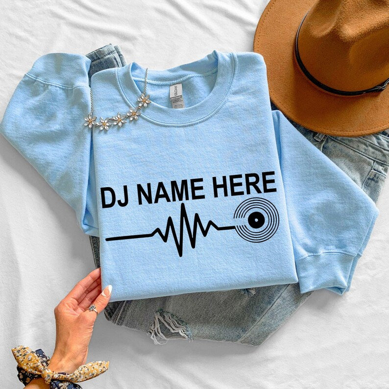 Express your passion for music with this personalised DJ Name Heartbeat Sweatshirt featuring a heartbeat waveform connected to a vinyl record. Whether performing behind the decks or relaxing with friends, this premium crewneck is professionally printed in the UK by TeezoraPrints.