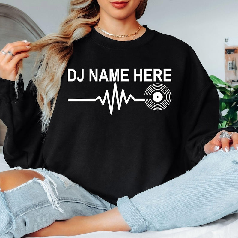 Personalised DJ Name Heartbeat Sweatshirt featuring a custom DJ name, heartbeat waveform and vinyl record graphic. Designed for DJs, music producers, club performers and electronic music lovers, this premium unisex crewneck is professionally printed in the UK by TeezoraPrints for exceptional comfort, warmth and everyday style.