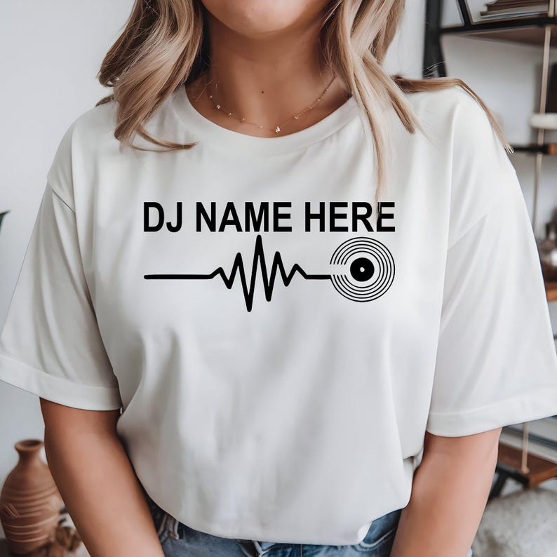 Personalised DJ Name Heartbeat T-Shirt featuring a custom DJ name, heartbeat waveform and vinyl record graphic. Designed for DJs, music producers, club performers and electronic music lovers who want a stylish personalised tee. Professionally printed in the UK by TeezoraPrints using premium-quality fabric for exceptional comfort, durability and everyday wear.