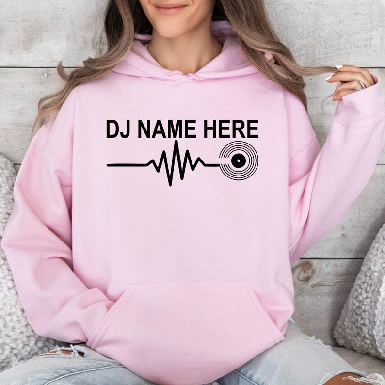 Featuring a custom DJ name, heartbeat waveform and vinyl record graphic, this personalised hoodie creates a clean modern look for DJs and music lovers. Professionally printed in the UK by TeezoraPrints using premium-quality materials.