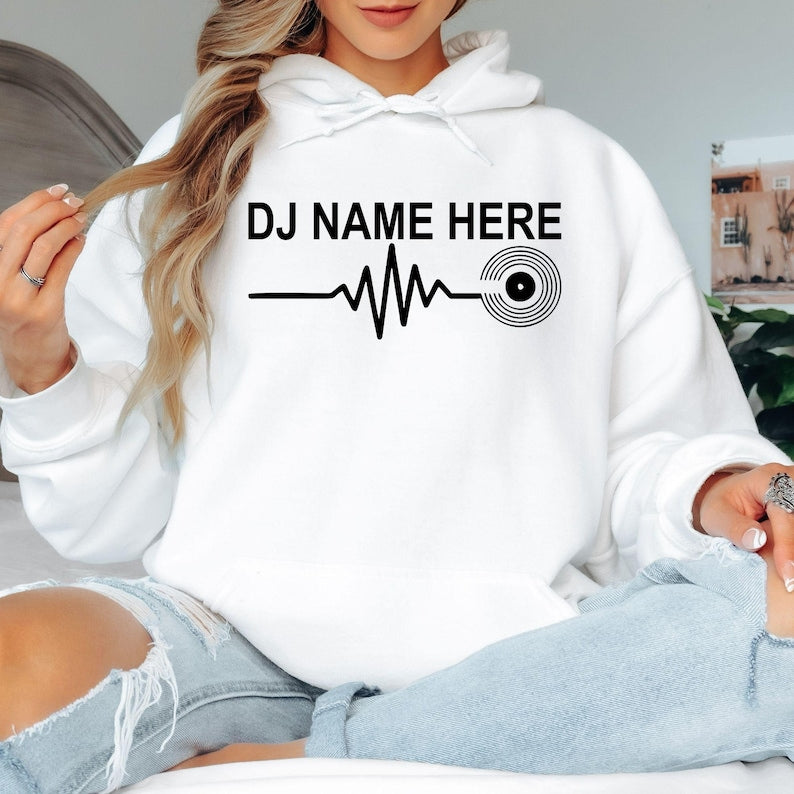 Personalised DJ Name Heartbeat Hoodie featuring a custom DJ name, heartbeat waveform and vinyl record graphic. Designed for DJs, music producers, club performers and electronic music lovers, this premium unisex hoodie is professionally printed in the UK by TeezoraPrints for warmth, comfort and everyday style.