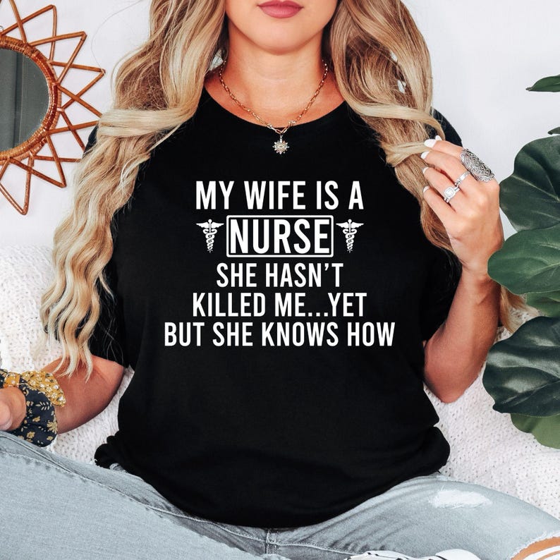 My Wife Is A Nurse She Hasn't Killed Me Yet But She Knows How T Shirt created for nurses, registered nurses, healthcare professionals, hospital staff, medical workers, supportive husbands, nursing families, and anyone who enjoys medical humour. Featuring bold nursing typography with medical symbols, this premium nurse-themed graphic tee from Teezora Prints delivers exceptional comfort, premium print quality, and stylish everyday fashion for proud nursing families.