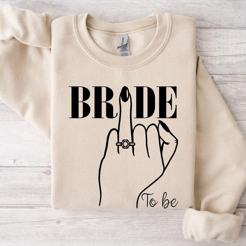 Looking for a thoughtful engagement gift? This Bride To Be sweatshirt is a meaningful keepsake for brides, fiancées and future wives celebrating their special journey. The elegant bridal illustration makes it a stylish gift for bridal showers, engagement celebrations and wedding preparations. Every sweatshirt is printed in the UK by TeezoraPrints using premium materials.