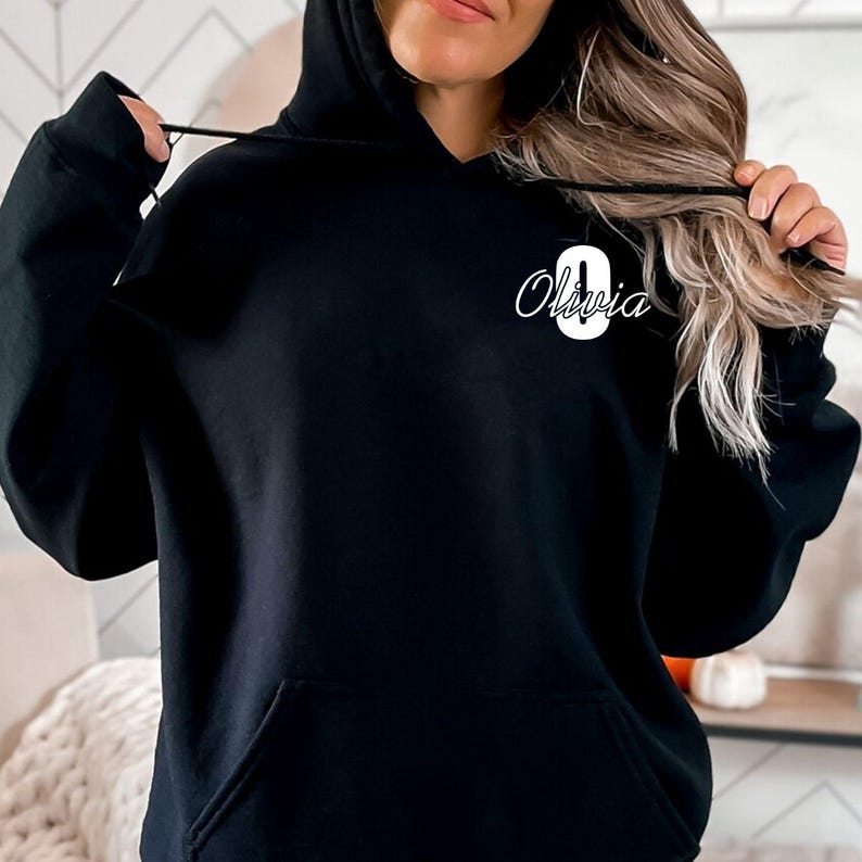 Personalised initial name hoodie featuring a large custom monogram letter combined with an elegant script name printed on the left chest area. This stylish custom hoodie offers a minimalist yet premium appearance, making it perfect for personalised fashion lovers seeking unique custom clothing. Professionally printed in the UK using durable high quality printing methods.