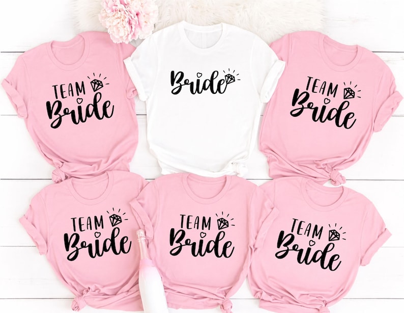 Personalised Team Bride shirt designed for brides, bridesmaids, maid of honour and every member of the bridal party. Featuring elegant script lettering with a sparkling engagement ring, this stylish bridal t-shirt is perfect for creating coordinated wedding outfits and memorable celebrations. Every shirt is professionally printed in the UK by TeezoraPrints using premium cotton for exceptional comfort and long-lasting quality.
