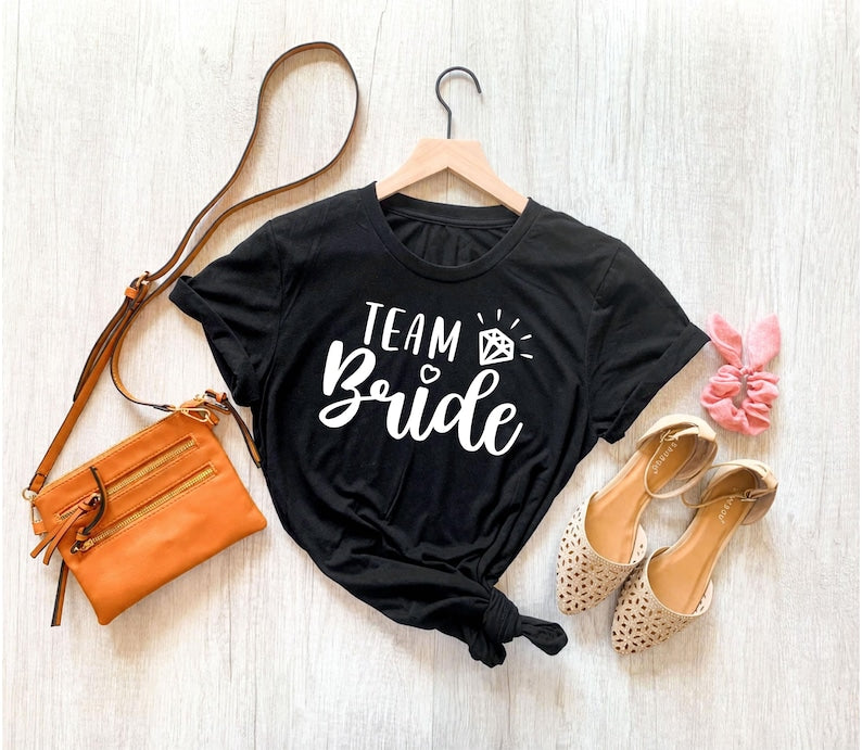Searching for a thoughtful bridal party gift? This Team Bride shirt is a beautiful keepsake for brides, bridesmaids, maid of honour and wedding party members. Designed with elegant typography and a sparkling engagement ring, every shirt is professionally printed in the UK by TeezoraPrints, making it a memorable gift for every wedding celebration.