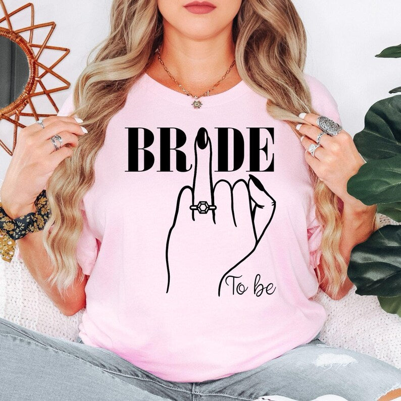 Bride To Be shirt with elegant engagement ring artwork for brides, fiancées and future wives. Ideal for bridal shower outfits, hen party clothing, engagement party shirts, wedding morning apparel, bridal gifts and wedding photoshoots. Every premium t-shirt is proudly printed in the UK by TeezoraPrints with outstanding print quality and comfort.
