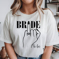 Personalised Bride To Be shirt featuring an elegant bride illustration, engagement ring design and stylish bridal typography. Perfect for bridal showers, hen parties, engagement celebrations, wedding mornings and bridal photoshoots. This premium bridal t-shirt is professionally printed in the UK by TeezoraPrints with vibrant colours, soft cotton fabric and long-lasting print quality.