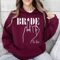 Bride To Be hoodie for brides, future wives and newly engaged women looking for stylish bridal clothing. Perfect for engagement celebrations, bridal showers, hen parties, wedding mornings, honeymoon travel and bridal weekends. Every premium hoodie is carefully printed in the UK by TeezoraPrints, offering outstanding quality, comfort and timeless style.