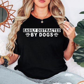 Easily Distracted By Dogs t shirt created for dog lovers, dog mums, dog dads, puppy parents, pet owners, animal rescuers, dog walkers, veterinarians, groomers, trainers, and anyone who instantly smiles whenever they see a dog. Featuring a bold typography design with cute paw prints, this premium graphic tee celebrates the special bond between people and their furry companions while delivering exceptional comfort, stylish everyday fashion, and a fun personality that every dog enthusiast will instantly relate