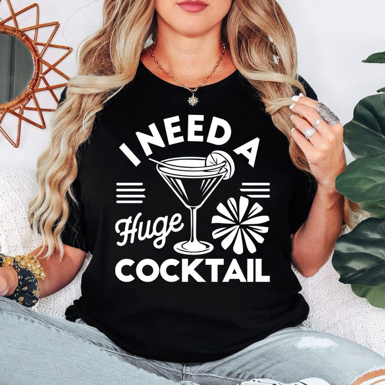 Funny cocktail t shirt designed for women who love cocktails, girls' nights out, brunch dates, weekend parties, and fun social events. Featuring the bold "I Need A Huge Cocktail" quote with a stylish cocktail glass graphic, this novelty tee is perfect for friends, sisters, wives, girlfriends, and cocktail enthusiasts who enjoy expressing their personality through humorous fashion. A comfortable statement shirt ideal for celebrations, holidays, and everyday casual wear.