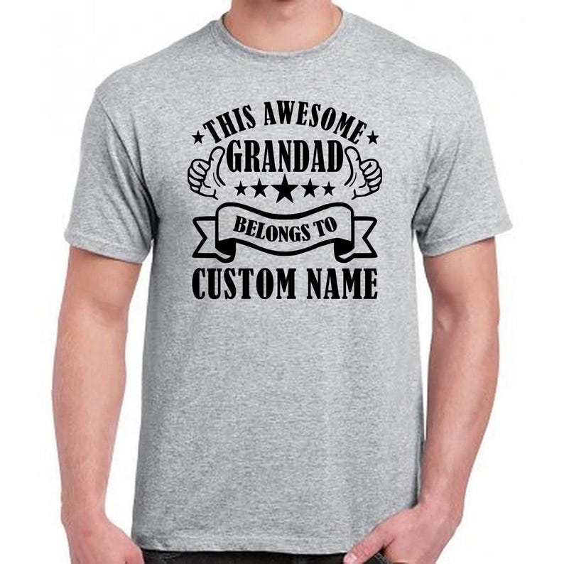 Family themed personalised grandad t shirt featuring “This Awesome Grandad Belongs To” typography with custom names and decorative graphic artwork. Meaningful unisex grandpa shirt designed for Fathers Day presents, Christmas gifting, birthday occasions and relaxed casual wear. Personalised family keepsake clothing for proud grandfathers who love sentimental gifts from children and grandchildren.