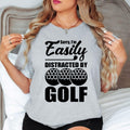 Teezora Prints Sorry I'm Easily Distracted By Golf T Shirt designed for golfers who think about golf every day, whether they're on the course, at the driving range, watching tournaments, or planning their next round. Featuring a bold typography layout with golf ball graphics, this premium graphic tee is perfect for golf enthusiasts, club members, weekend players, retirees, sports lovers, and anyone proud to show their passion for golf. Ideal for holidays, golf trips, club events, birthdays, Father's Day, re