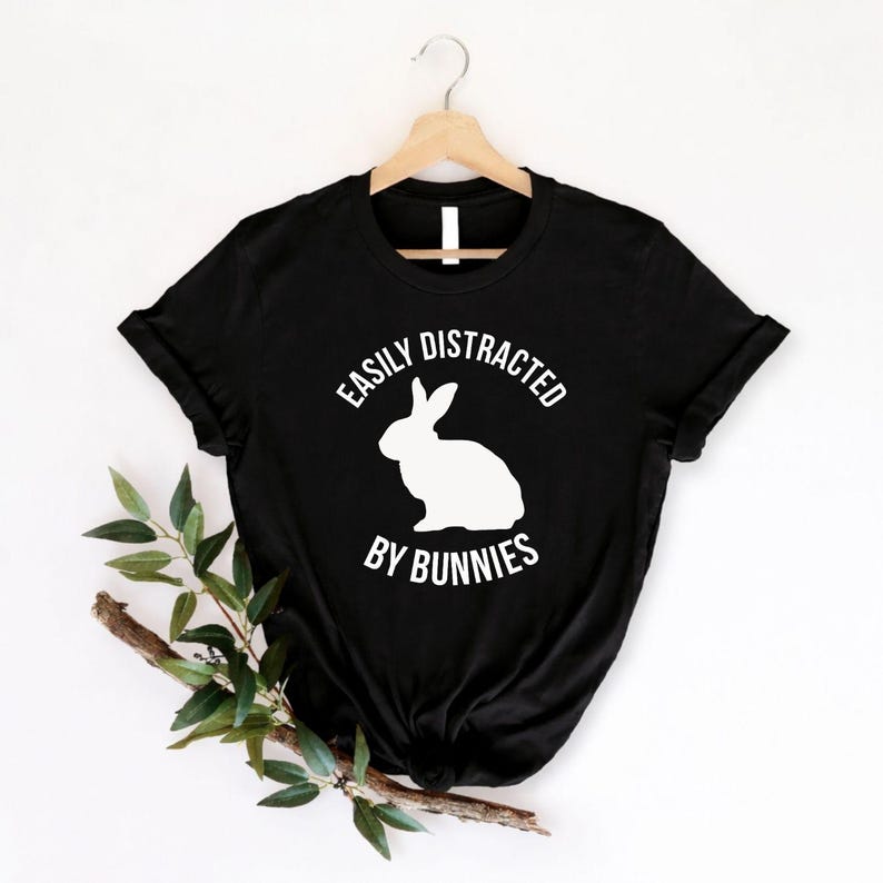 Easily Distracted By Bunnies T Shirt created for bunny lovers, rabbit owners, pet parents, animal enthusiasts, rabbit breeders, rescue volunteers, farm lovers, veterinary staff, and anyone who instantly smiles whenever they see a bunny. Featuring a bold rabbit silhouette with clean typography, this premium graphic tee from Teezora Prints celebrates a love for adorable rabbits while delivering exceptional comfort, premium print quality, stylish everyday fashion, and a fun personality for every bunny enthusia