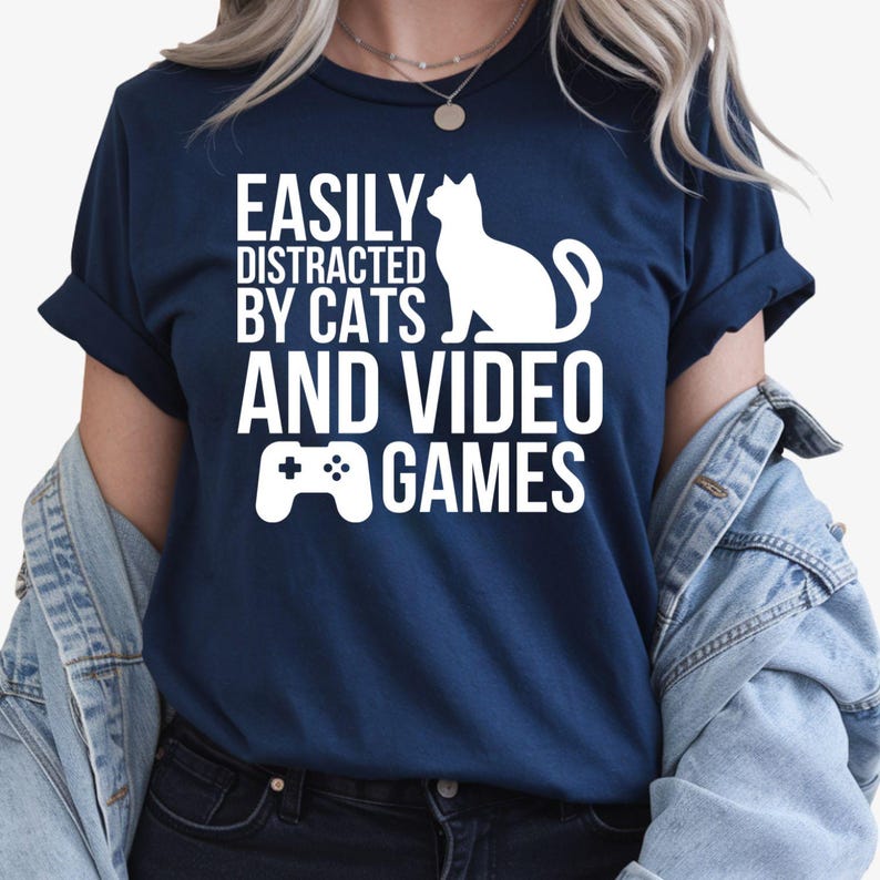 Funny Gamer Shirt, Easily Distracted By Cats And Video Games Shirt, Cat Lover T Shirt, Gaming Shirt, Video Game Tee, Cat Graphic Shirt, Gamer Gift, Gaming Controller Tee, PC Gamer Shirt, Console Gamer Tee, Cat Mum Shirt, Cat Dad Shirt, Funny Cat Shirt, Gaming Apparel, Animal Lover Tee, Premium Graphic T Shirt by Teezora Prints, Gamer Clothing, Cat Lover Gift, Gaming Fashion, Casual Gamer Tee, Video Game Lover Shirt, Esports Shirt, Cat Owner Apparel, Gamer Lifestyle Shirt.