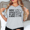 Easily Distracted By Cats & Books T Shirt is designed for people who believe the perfect day includes a good book and a cuddly cat. Whether you're reading novels, visiting bookstores, relaxing with your pet, enjoying quiet weekends, or building your home library, this premium graphic tee from Teezora Prints reflects your personality. Featuring a charming sleeping cat illustration on stacked books, it's ideal for everyday casual wear, holidays, travel, and every proud bookworm who loves cats.