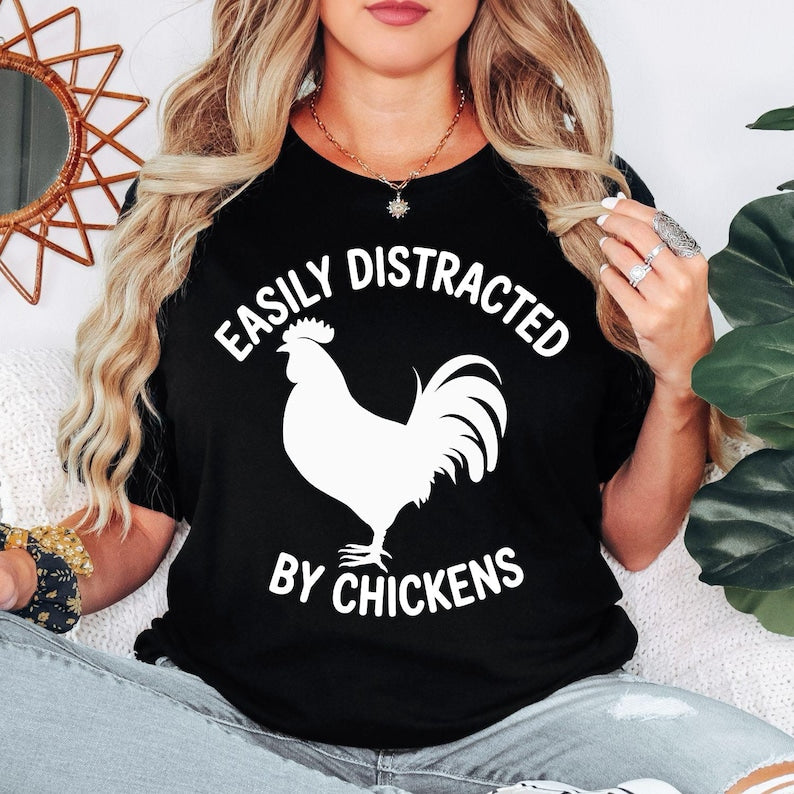 Easily Distracted By Chickens T Shirt created for chicken lovers, backyard chicken keepers, poultry farmers, homesteaders, smallholders, country lifestyle enthusiasts, farm animal lovers, rural families, and anyone who can't resist stopping to admire chickens. Featuring a bold chicken silhouette with modern typography, this premium graphic tee from Teezora Prints celebrates farm life while offering exceptional comfort, premium print quality, stylish everyday fashion, and a fun personality for poultry enthus