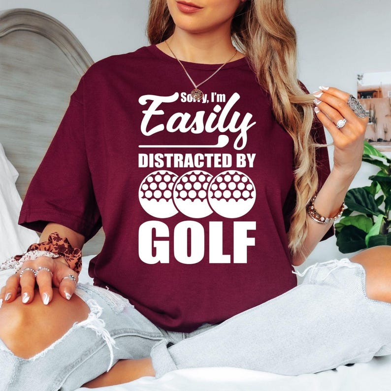 Teezora Prints Funny golf t shirt featuring the quote Sorry I'm Easily Distracted By Golf with bold typography and golf ball graphics designed for golfers and sports enthusiasts. Ideal for customers searching golf lover shirts, funny golfer tees, golf player clothing, golf tournament apparel, golf gifts for men and women, golf club fashion, weekend golfer outfits, premium golf graphic t shirts, golf lifestyle apparel, and unique golf clothing with modern typography.