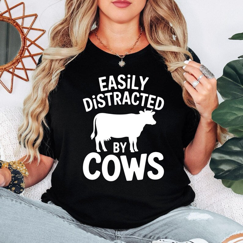 Funny Easily Distracted by Cows shirt designed for cow lovers, farmers, ranchers, dairy workers and anyone who enjoys country life. Featuring a bold cow silhouette and playful slogan, this premium graphic t-shirt is perfect for everyday wear on the farm or in town. Professionally printed in the UK by TeezoraPrints, offering exceptional comfort, quality and long-lasting durability for every animal enthusiast.