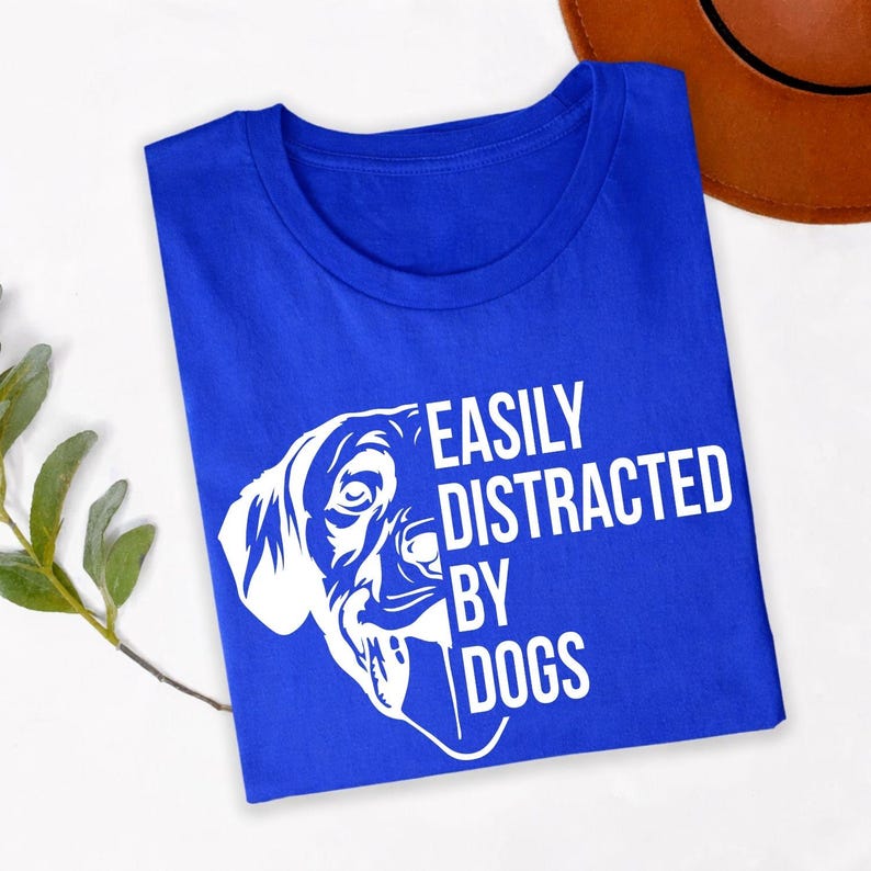 Perfect for dog walks, pet adoption events, dog training classes, animal rescue fundraisers, pet expos, countryside holidays, family outings and casual everyday wear. This Easily Distracted by Dogs shirt combines humour with comfort, while every premium t-shirt is professionally printed in the UK by TeezoraPrints for long-lasting quality and vibrant detail.
