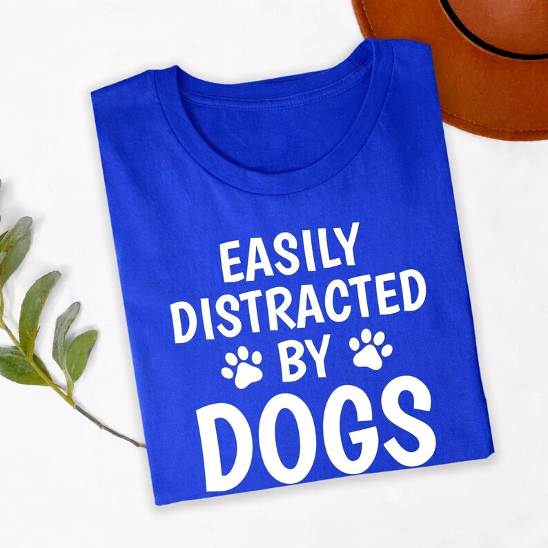 Perfect for dog walks, pet adoption days, dog training classes, animal rescue events, pet expos, countryside holidays, family outings and casual everyday wear. This Easily Distracted by Dogs shirt combines comfort, humour and style, while every premium t-shirt is professionally printed in the UK by TeezoraPrints using high-quality materials.
