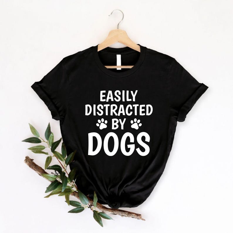 Perfect for dog lovers, pet parents, puppy owners and animal enthusiasts, this Easily Distracted by Dogs shirt features bold typography with adorable paw prints, making it a fun everyday choice. Whether you're walking your dog, visiting the park or relaxing with your favourite companion, this premium graphic tee offers lasting comfort. Professionally printed in the UK by TeezoraPrints using high-quality materials.