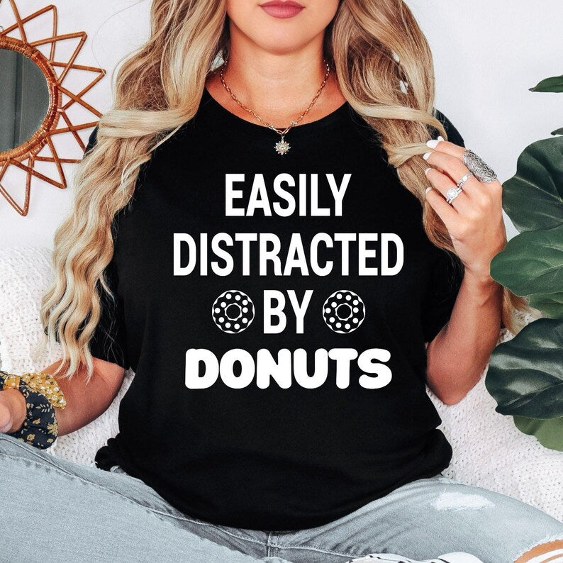 Perfect for donut lovers, bakers, foodies and anyone with a serious sweet tooth, this Easily Distracted by Donuts shirt features bold typography with playful donut graphics for a fun everyday look. Ideal for casual outings, bakery visits and coffee dates. Every premium t-shirt is professionally printed in the UK by TeezoraPrints using high-quality materials for exceptional comfort.