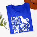 Easily Distracted By Cats And Video Games T Shirt is made for people whose ideal day includes playing video games while spending time with their favourite cat. Whether you're grinding ranked matches, relaxing with indie games, watching esports, or cuddling your pet after a gaming session, this premium graphic tee from Teezora Prints perfectly represents your personality. Featuring a bold cat silhouette and gaming controller design, it's ideal for everyday wear, travel, gaming events, holidays, and casual st