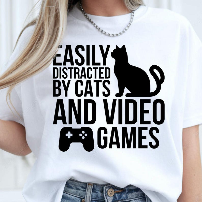 Easily Distracted By Cats And Video Games T Shirt created for cat lovers, gamers, streamers, console players, PC gamers, pet parents, esports fans, and anyone whose two greatest passions are cats and gaming. Featuring a playful cat silhouette with a game controller, this premium graphic tee from Teezora Prints delivers exceptional comfort, professional print quality, stylish everyday fashion, and the perfect conversation starter for gaming and feline enthusiasts alike.