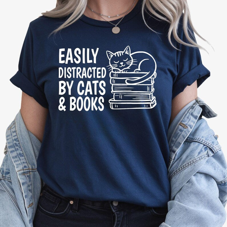 Looking for the perfect gift for someone who loves books and cats? This Easily Distracted By Cats & Books T Shirt from Teezora Prints features an adorable sleeping cat resting on a stack of books with bold typography that every reader will instantly love. Professionally printed on a premium quality unisex t shirt, it offers exceptional comfort, long-lasting durability, and timeless style. Perfect for birthdays, Christmas, Book Club gifts, Teacher Appreciation, Mother's Day, and thoughtful surprises for read