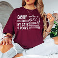 Easily Distracted By Cats & Books T Shirt featuring a cute sleeping cat on stacked books designed for bookworms, readers, librarians, teachers, students, and cat lovers. Teezora Prints creates premium apparel for customers searching book lover shirts, cat lover clothing, reading t shirts, library apparel, bookworm gifts, literary fashion, reading quote shirts, cat graphic tees, premium book-themed clothing, and unique gifts for passionate readers.