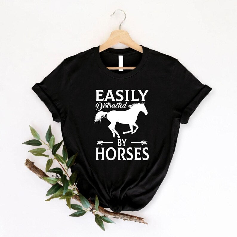 Celebrate your love for horses with this Easily Distracted by Horses shirt featuring a running horse silhouette and bold typography. Whether you're riding, caring for horses, exploring the countryside or spending time at the barn, this premium t-shirt delivers comfort and timeless style. Every shirt is proudly printed in the UK by TeezoraPrints.