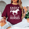 Show your passion for horses with this Easily Distracted by Horses graphic t-shirt featuring a detailed running horse silhouette and eye-catching typography. The soft premium cotton and relaxed unisex fit make it perfect for everyday wear, riding events and country adventures. Every order is made to order and professionally printed in the UK by TeezoraPrints.