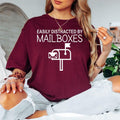 Bring humour to your wardrobe with this Easily Distracted by Mailboxes graphic t-shirt featuring a clean mailbox illustration and bold lettering. The comfortable unisex fit and premium cotton fabric make it ideal for work or everyday wear. Every order is made to order and professionally printed in the UK by TeezoraPrints for exceptional quality.