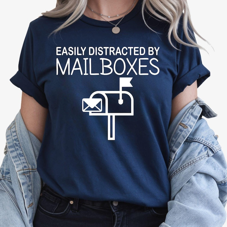 Perfect for postal workers, mail carriers, mailbox collectors and anyone who enjoys quirky everyday humour, this Easily Distracted by Mailboxes shirt features a bold mailbox graphic with a playful slogan. Ideal for workdays, casual wear or showing your love for all things postal. Every premium t-shirt is professionally printed in the UK by TeezoraPrints using high-quality materials.