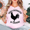 Easily Distracted By Chickens T Shirt featuring a bold rooster silhouette and funny poultry quote designed for chicken keepers, farmers, homesteaders, and animal lovers. Teezora Prints creates premium apparel for customers searching chicken lover shirts, rooster clothing, backyard chicken t shirts, poultry gifts, country lifestyle apparel, farm graphic tees, rural fashion, homestead clothing, premium chicken apparel, and unique farm-themed casual wear.