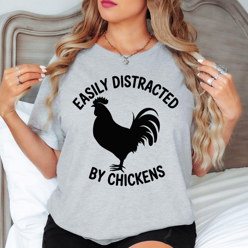Easily Distracted By Chickens T Shirt is designed for people who love collecting fresh eggs, caring for backyard chickens, living the homestead lifestyle, and enjoying peaceful country mornings. Featuring a bold rooster silhouette with clean typography, this premium graphic tee from Teezora Prints perfectly reflects a passion for poultry, farming, and rural life. Ideal for everyday casual wear, farm work, weekend markets, countryside holidays, travel, and anyone proud to show their love for chickens.